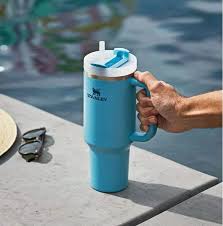 Blue insulated tumbler with handle held by a hand by a poolside.
