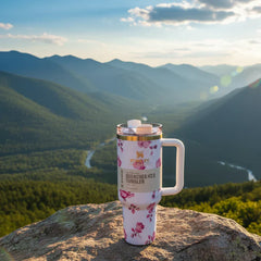 Floral-patterned tumbler on a rock with a mountainous landscape in the background
