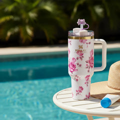 Floral-patterned tumbler with straw on a table by a pool