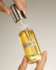 La Mer skincare serum bottle held by a hand against a neutral background