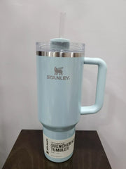 Light blue Stanley tumbler with handle on a wooden surface and light gray background