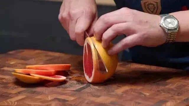 Person slicing a grapefruit on a wooden cutting board