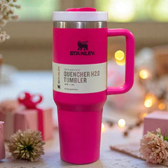 Pink Stanley Quencher H2O tumbler on a decorative surface with blurred lights and flowers in the background.
