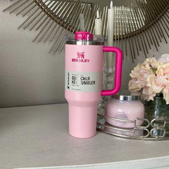 Pink Stanley tumbler with a gray label on a surface with decorative elements.