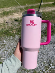 Pink Stanley tumbler with a handle held in a hand outdoors.