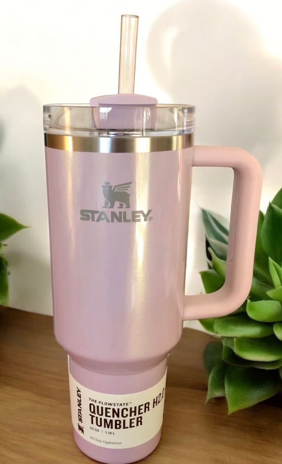Pink Stanley tumbler with a handle on a wooden surface with plants in the background