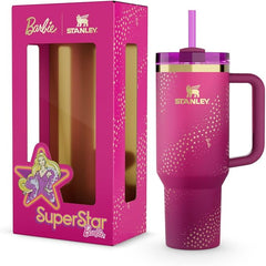 Pink Stanley tumbler with handle and straw lid, featuring Barbie branding, next to its packaging.