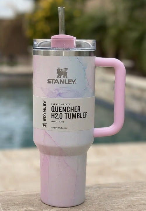 Pink marbled tumbler with handle and straw lid on a wooden surface, Stanley branding visible.