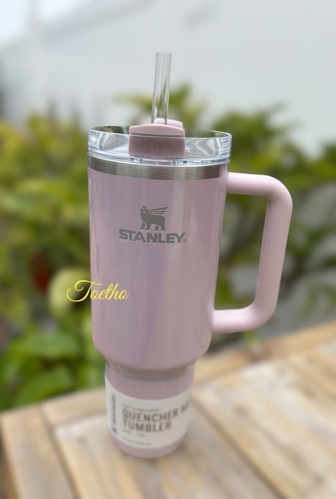 Pink tumbler with handle on a wooden surface, blurred greenery in the background