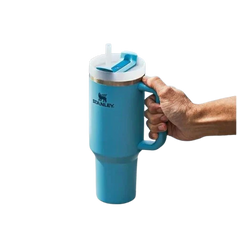 Turquoise Stanley mug with handle held by a hand on a white background
