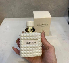 White Valentino perfume bottle held by a hand with a matching box in the background.